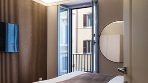 Une chambre d’hôtel avec un lit, un téléviseur fixé au mur, un mur recouvert de panneaux en bois et une vue sur le balcon extérieur.
