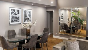 Un espace repas moderne avec une table en verre, des chaises à revêtement gris et des photographies en noir et blanc encadrées accrochées au mur.