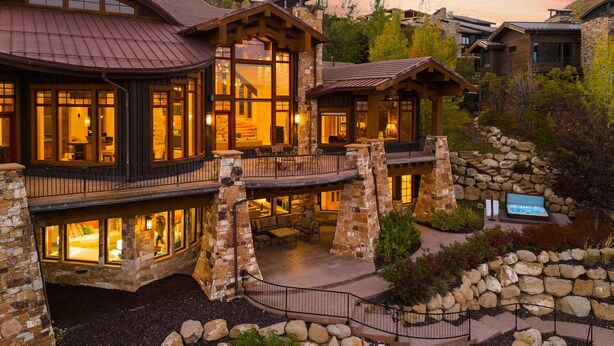 A multi-level stone building with balconies, large windows, and a hot tub in the garden.