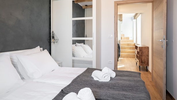 A modern hotel room with a bed, a walk-in closet, and a wooden staircase leading to a balcony. - Blue Sky Duplex (Piran)
