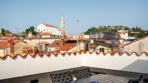 A rooftop terrace with a table and chairs, overlooking a cityscape with historic buildings and a hill with a castle. - Blue Sky Duplex (Piran)