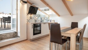A modern kitchen with a skylight, wooden beams, and a dining area with a table and chairs. - Blue Sky Duplex (Piran)
