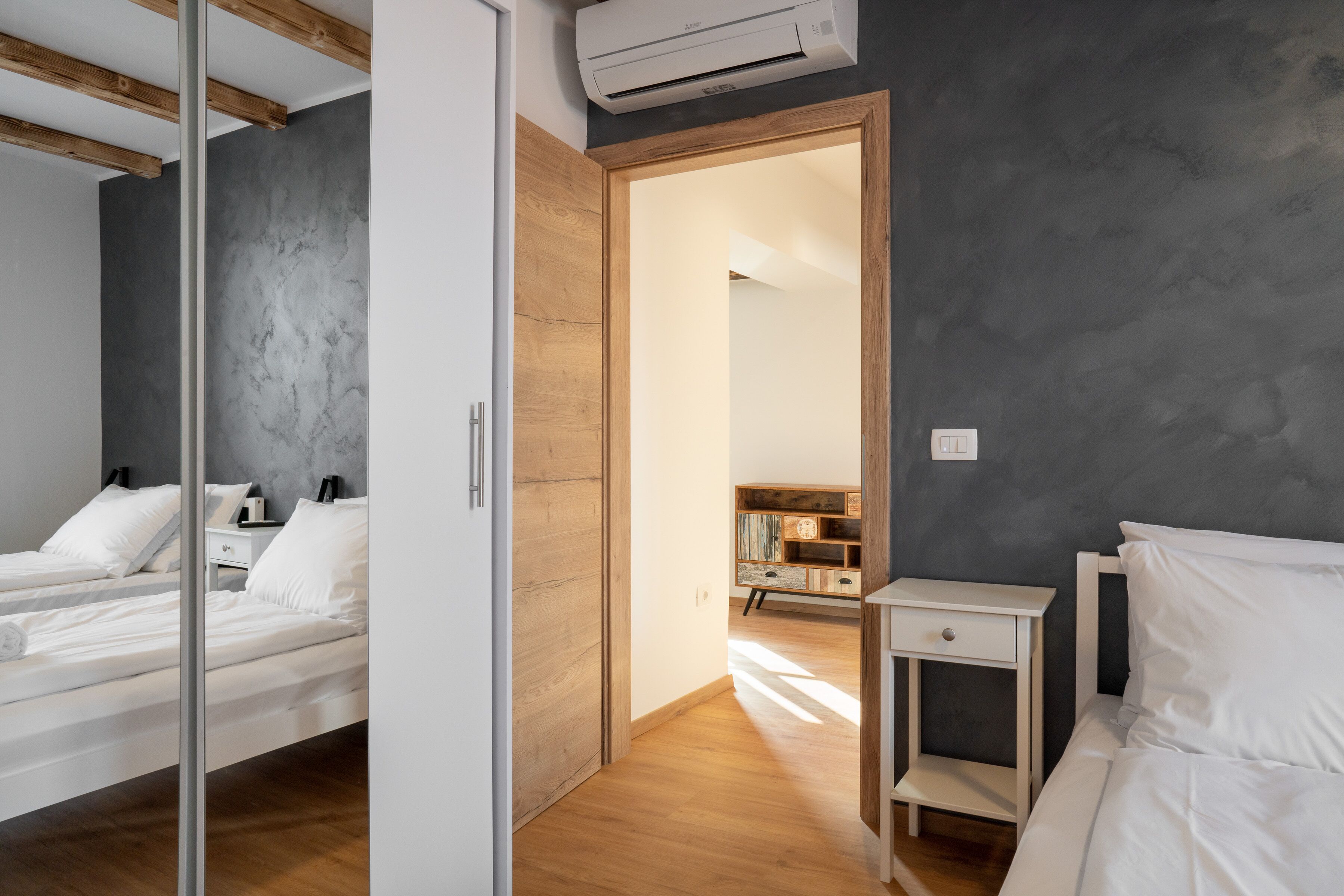 A modern bedroom with a wooden wardrobe, a bedside table, and a bed with white bedding.