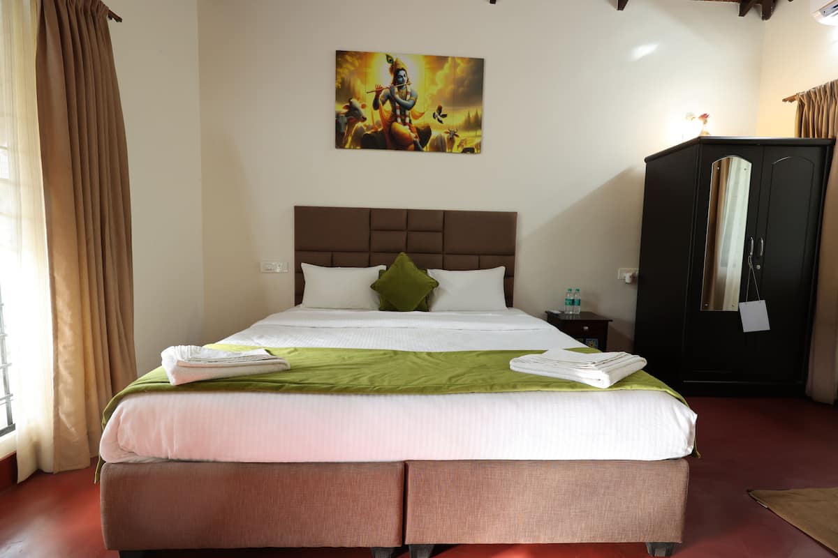 A neatly made bed with a green throw blanket and white pillows, a headboard, a nightstand with a lamp, and a painting on the wall.