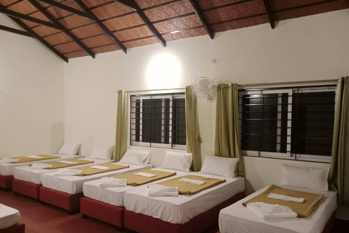 A hotel room with four beds arranged in a row, each with white linens and brown headboards.