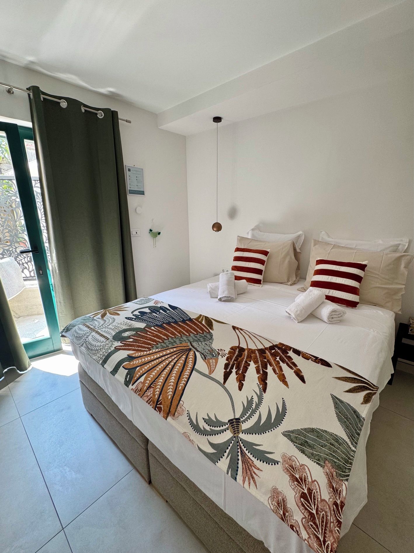 Ein Hotelzimmer mit Bett, Kissen, Vorhang, Wandlampe und Tür.
