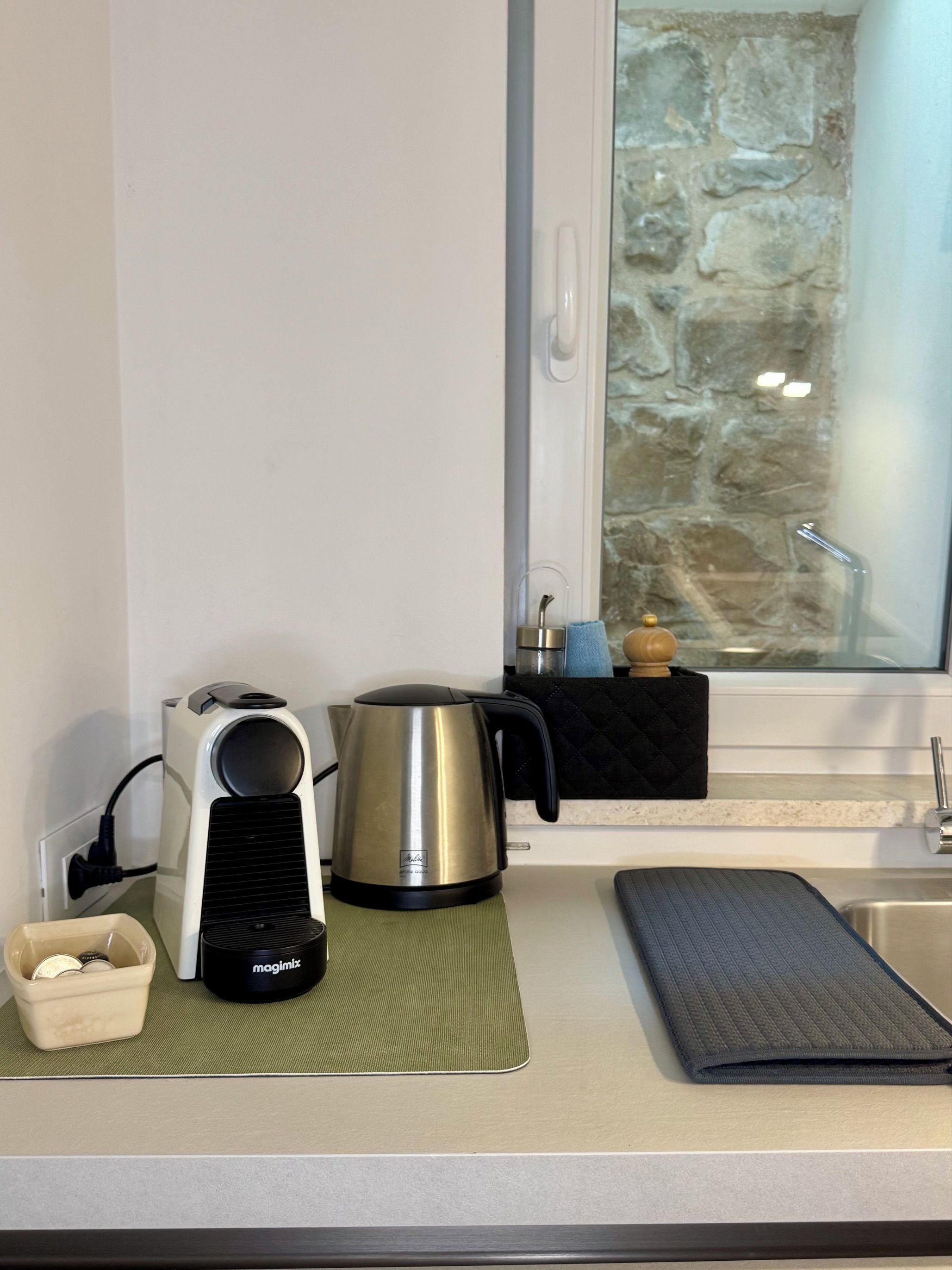 A kitchen with a kettle, a coffee maker, and a mat on the counter.