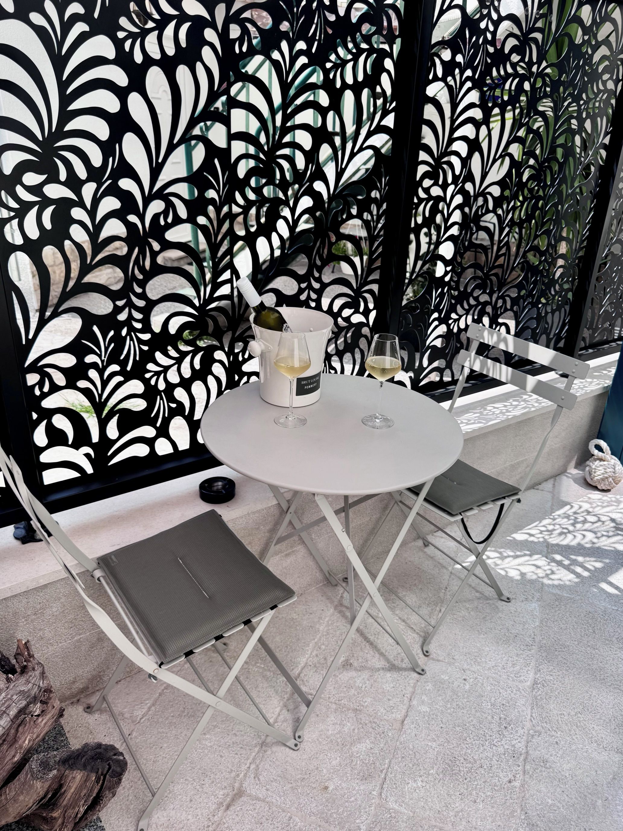 A round table with two chairs, a bottle of wine, and glasses on it.