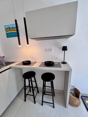 A modern kitchen with a white countertop, two black stools, a hanging painting, and a black lamp.