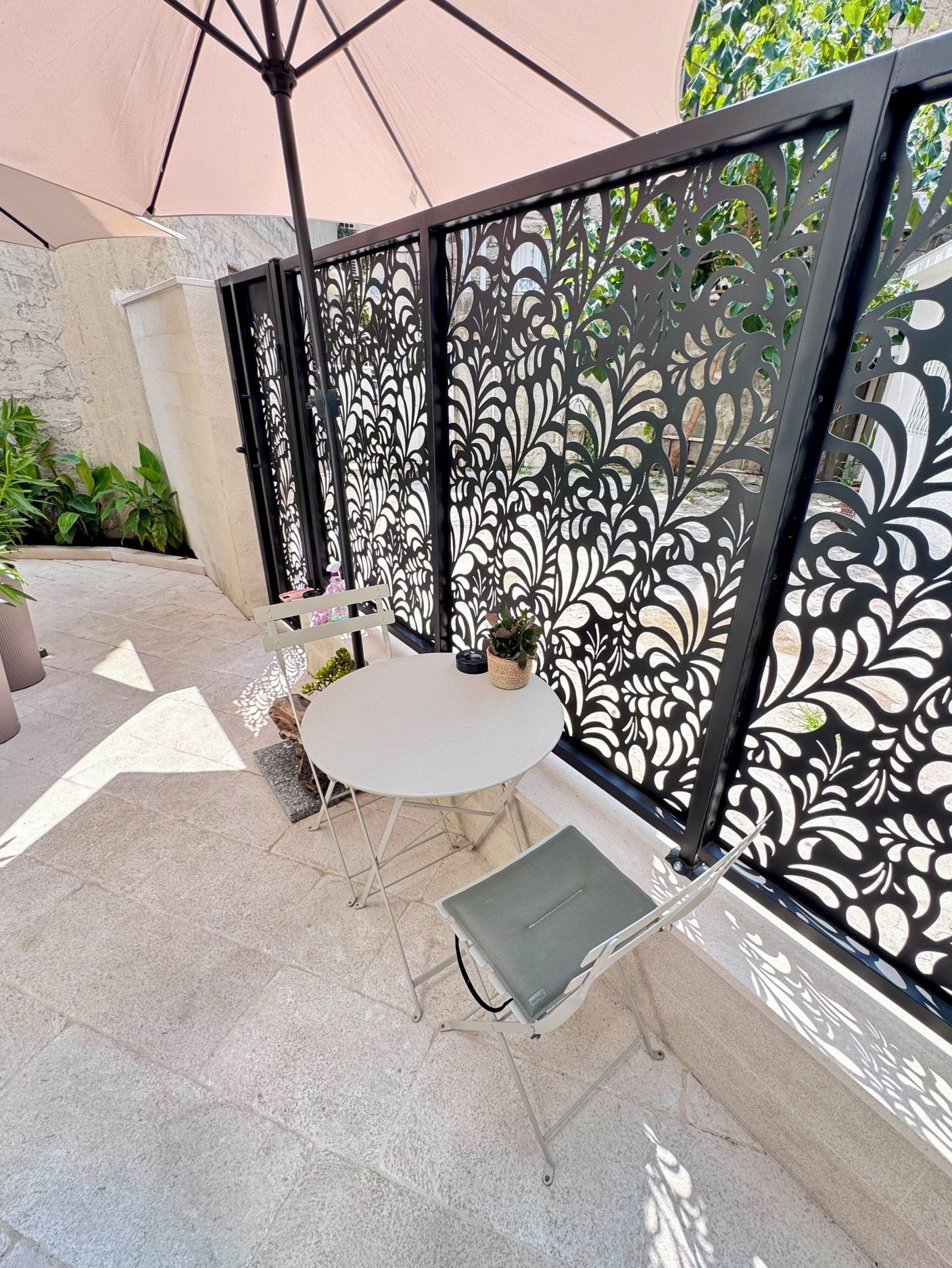 A patio area with a round table and a chair, a decorative metal fence, and potted plants.