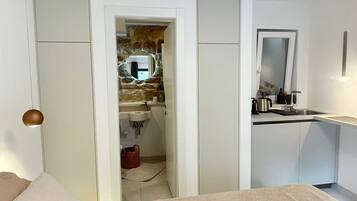 Una camera d'albergo compatta con un letto, un angolo cottura, un bagno con parete in pietra e uno specchio.