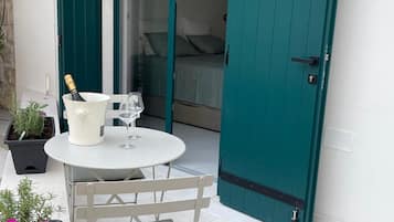 A small outdoor seating area with a table and chairs, a bottle of champagne, and potted plants.