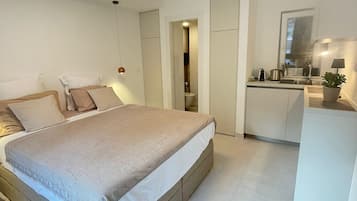 Una camera da letto moderna con un letto grande, un angolo cottura piccolo e un bagno visibile attraverso una porta aperta.