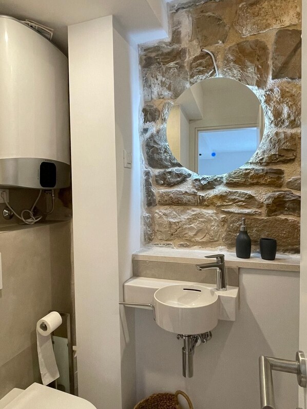 A bathroom with a stone wall, a sink, a mirror, and a toilet.