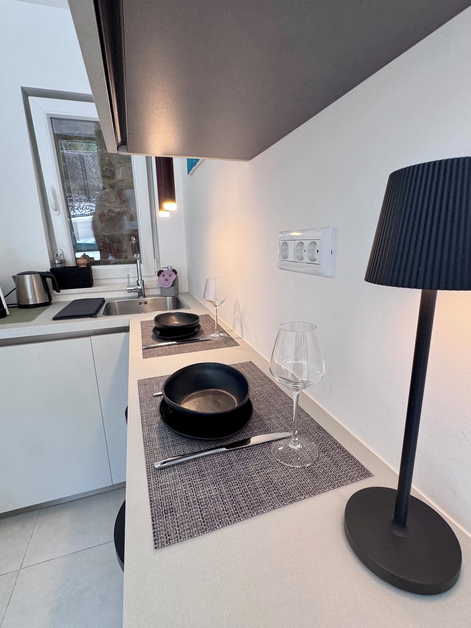 Eine moderne Küche mit einer zentralen Kochinsel, einem Wasserkocher, einem Weinglas und einer Lampe.