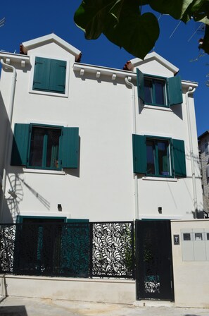 A two-story building with green shutters, a white facade, and a decorative metal gate.