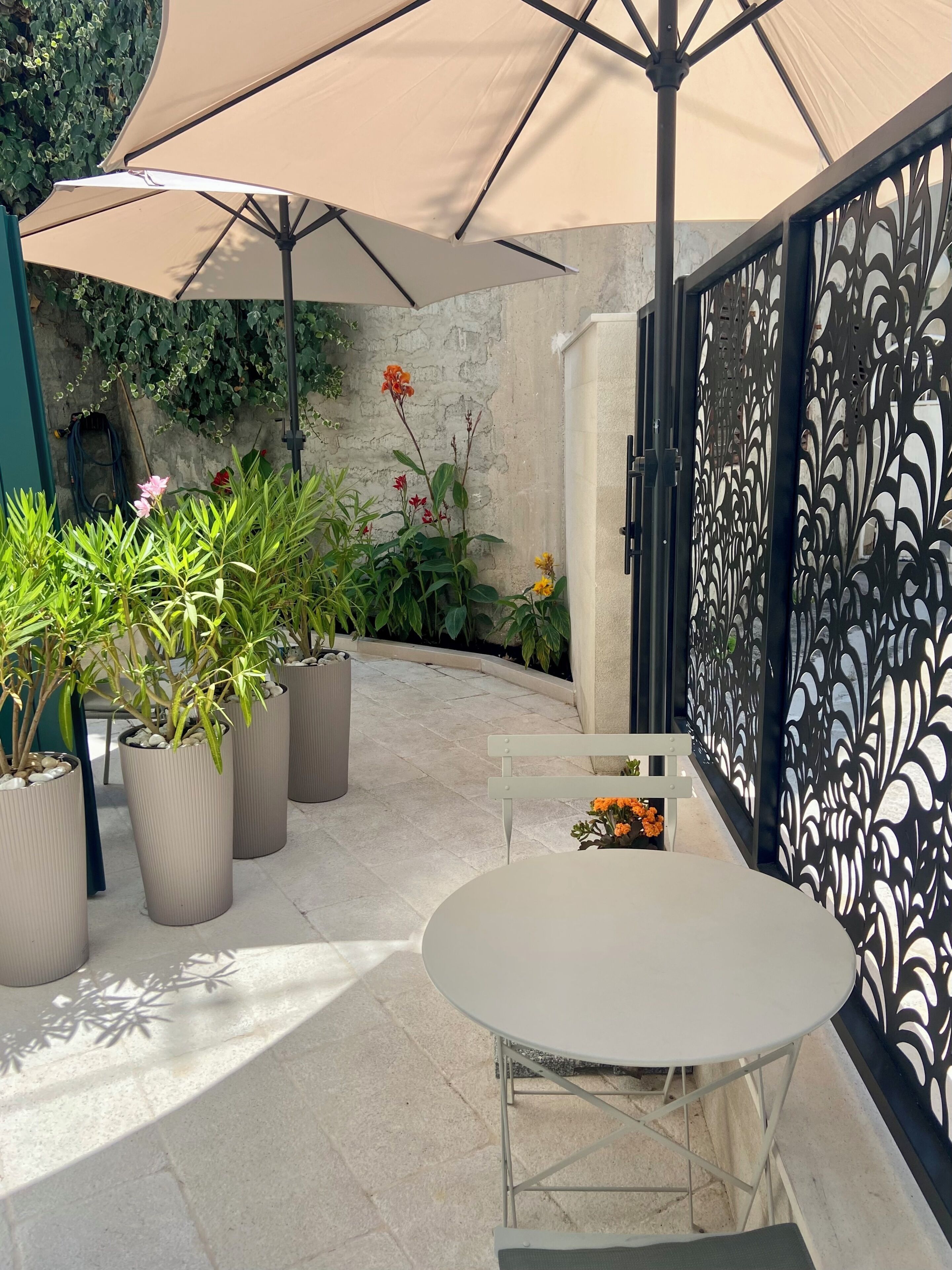 An outdoor patio with a round table and chairs, surrounded by potted plants and a decorative fence.