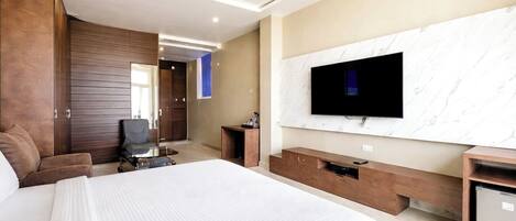 A modern hotel room with a large bed, a flat-screen TV mounted on a marble wall, a desk with a chair, and a ceiling fan.