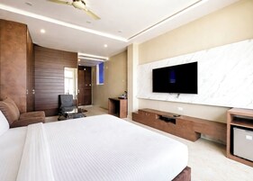 Camera d'albergo moderna con un letto grande, una TV a schermo piatto montata su una parete in marmo, una scrivania con una sedia e una ventola a soffitto.
