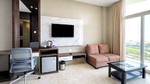 A modern hotel room with a flat-screen TV mounted on a marble wall, a sofa, a desk with a chair, a coffee maker, and a trash can. - The Sea View Suites - Sea front, Pool & Breakfast (Puri)