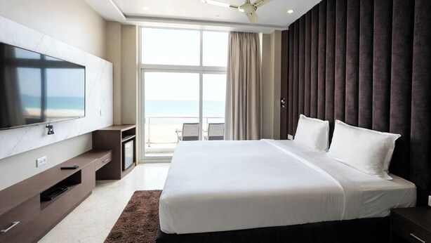 A modern hotel room with a large bed, a flat-screen TV, a ceiling fan, and a view of the ocean. - The Sea View Suites - Sea front, Pool & Breakfast (Puri)