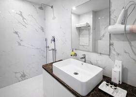 Un baño moderno con pared de mármol, un lavamanos blanco, un cabezal de ducha de mano, un perchero y un secador de pelo.