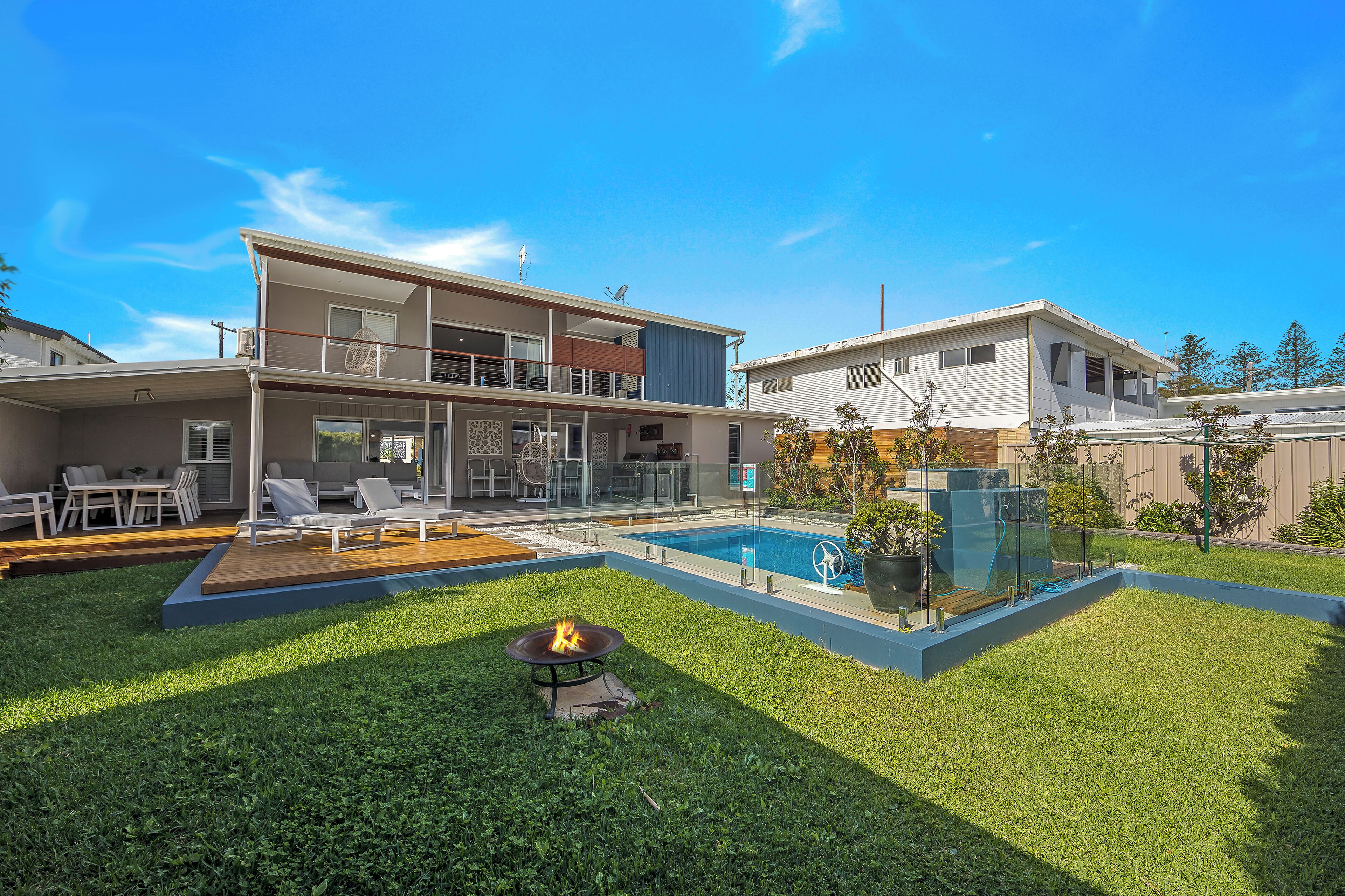 Une maison moderne à deux étages dotée d’une piscine, d’un espace salon extérieur et d’un foyer.