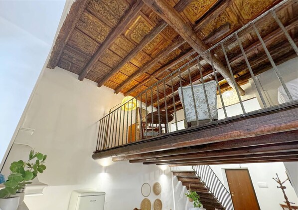 Un intérieur à plusieurs niveaux avec un escalier en bois, un balcon doté d’une rambarde en métal et un mur blanc orné d’assiettes décoratives.