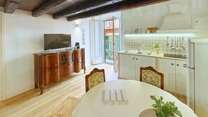Un comedor con una mesa y sillas de madera, un televisor sobre un mueble de madera, y una zona de cocina con un fregadero y armarios.