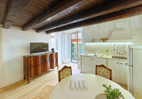 A dining area with a wooden table and chairs, a television on a wooden cabinet, and a kitchen area with a sink and cabinets. - Solemar Sicilia - Casa Enrica (Palermo)
