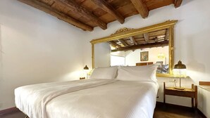 Una cama bien tendida con sábanas blancas en una habitación con techo de madera y un espejo grande arriba.