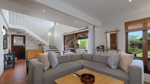 A spacious living room with a grey sectional sofa, a wooden coffee table, and a staircase leading to an upper level.