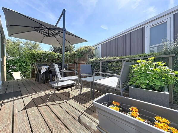 Une terrasse dotée de mobilier d’extérieur, d’un grand parasol et de plantes en pot.