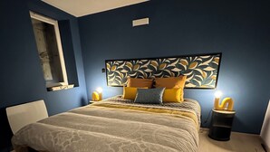 Ein Schlafzimmer mit einem Bett, einem Blattmuster-Kopfschild, Nachttischlampen und einem Fenster.