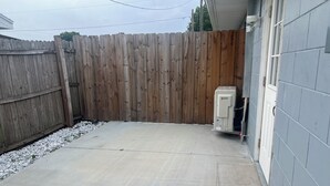 A backyard with a concrete patio, a wooden fence, and a utility box near the house. - Cozy Haven Apartment (Winter Haven)