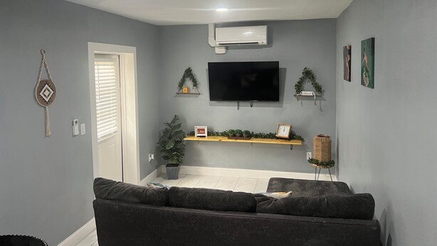 A living room with a grey sofa, a flat-screen TV, and a small plant on a shelf. - Cozy Haven Apartment (Winter Haven)