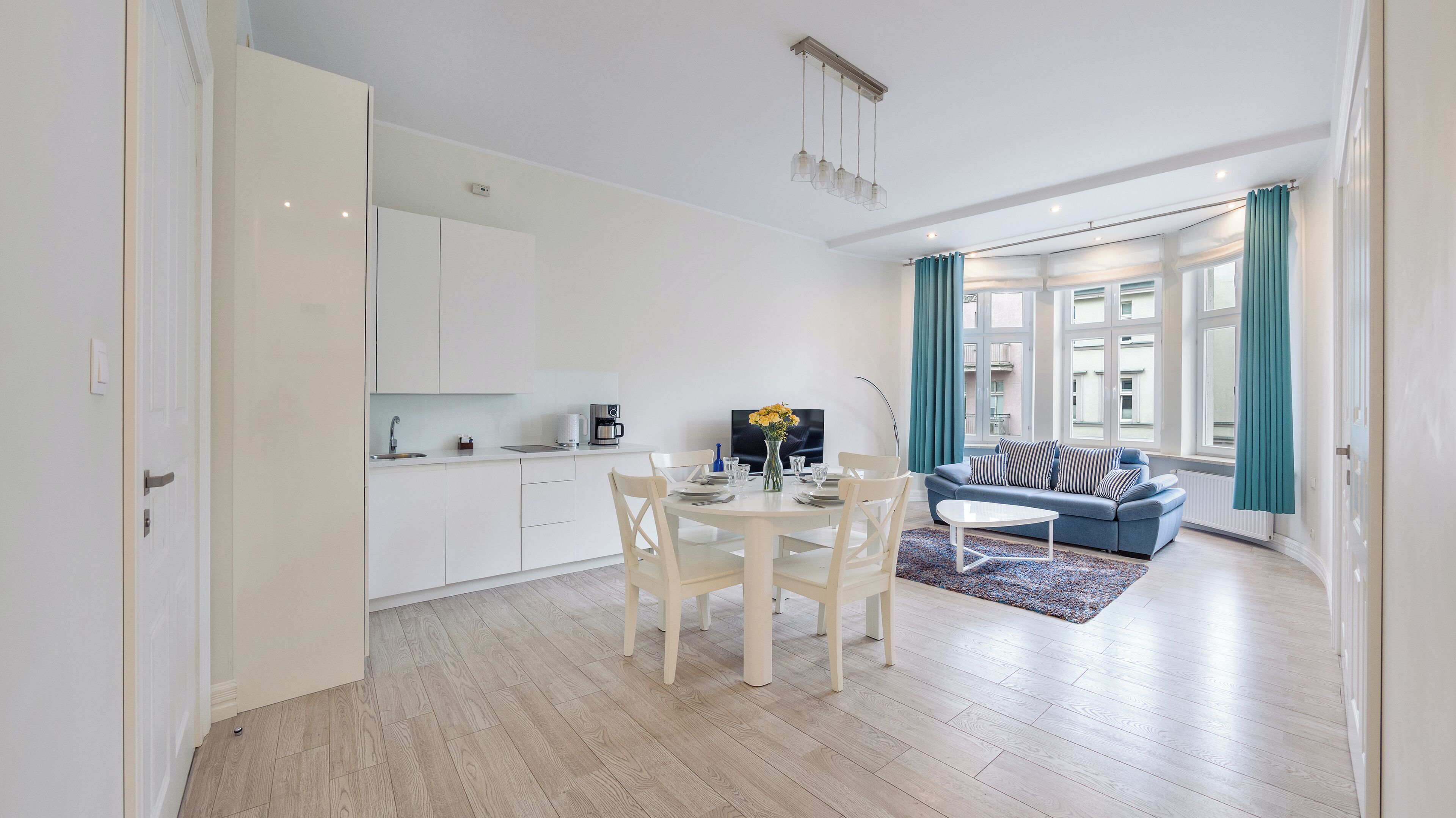 A modern living space with a dining area, a kitchen, and a seating area with a sofa and curtains.