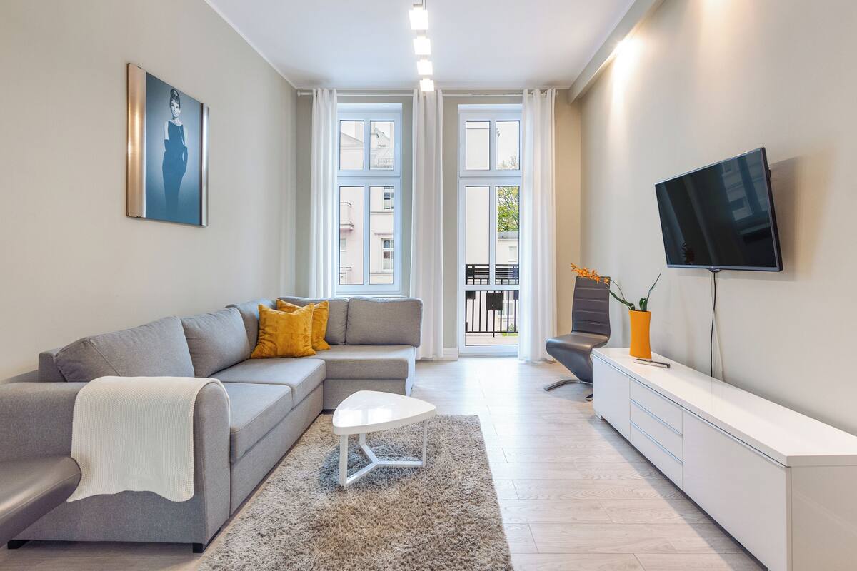 Una sala moderna con un sofá seccional gris, una mesa de centro blanca y un televisor de pantalla plana montado en la pared.