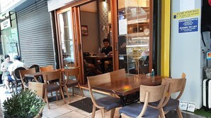 An outdoor seating area with wooden tables and chairs, a potted plant, and a glass door entrance. - Glamorous & Spacious Renovated Apartment, Syntagma (Athina)