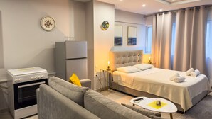 A hotel room with a bed, a sofa, a small table, a lamp, a refrigerator, and a wall-mounted plate. - Glamorous & Spacious Renovated Apartment, Syntagma (Athina)