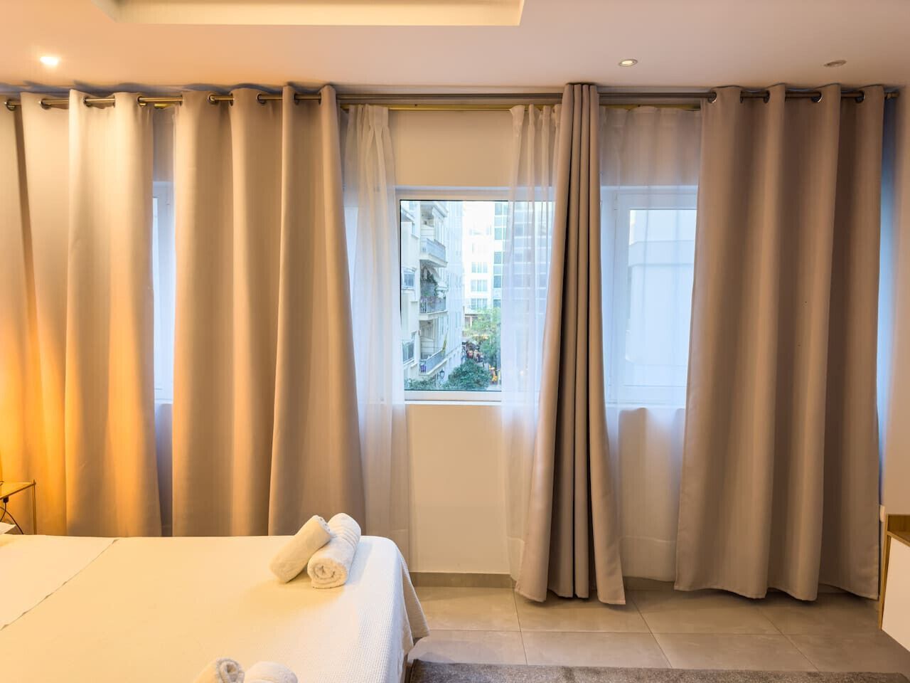 A hotel room with a bed, curtains, and a window with a view of buildings.