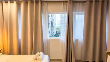 A hotel room with a bed, curtains, and a window with a view of buildings.