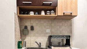 A kitchen with a sink, wooden cabinets, a coffee machine, and a dish rack.