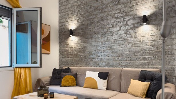 A modern living room with a brick-patterned wall, a sofa with cushions, a coffee table, and a floor lamp.