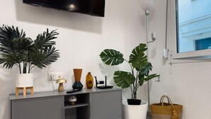 A modern living room with a grey cabinet, a mounted TV, and two large potted plants.