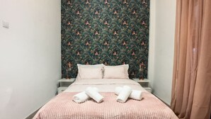A neatly made bed with a pink bedspread and pillows, a patterned wallpaper headboard, and a curtain on the right side.