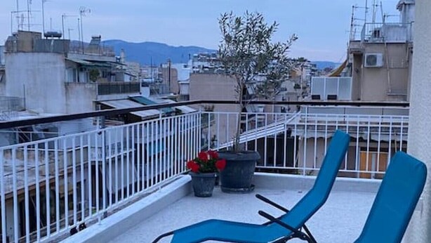 Una terrazza sul tetto con due poltrone blu, una pianta in vaso e un tavolino con fiori rossi.