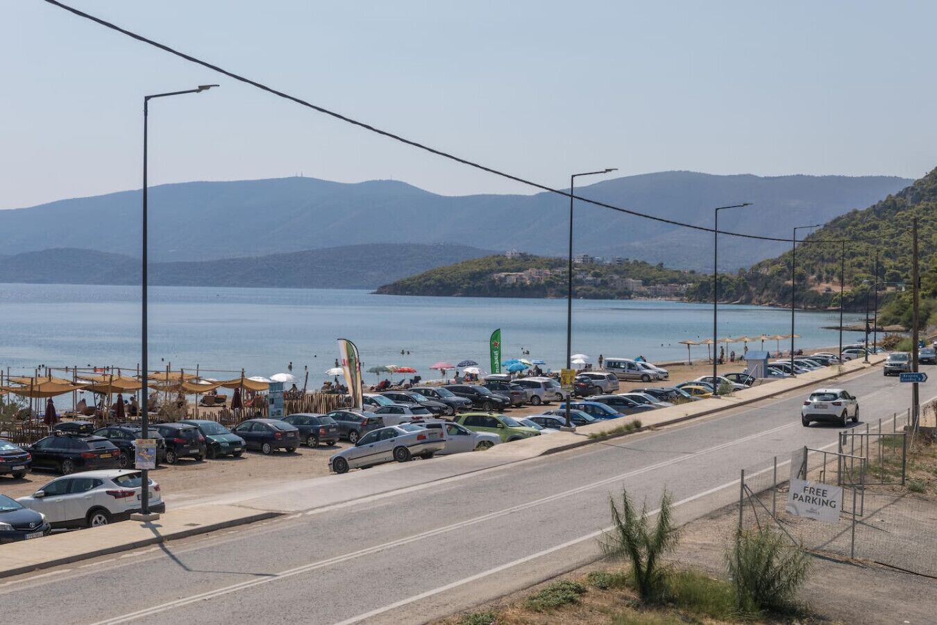 Eine Küstenstraße mit parkenden Autos, freier Meerblick und Bergen im Hintergrund.