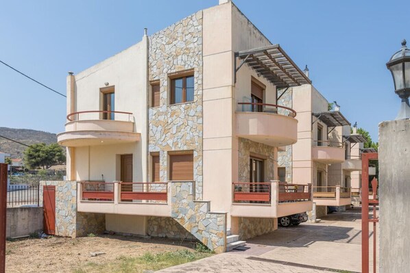 A modern two-story residential building with a stone facade, balconies, and a paved driveway.