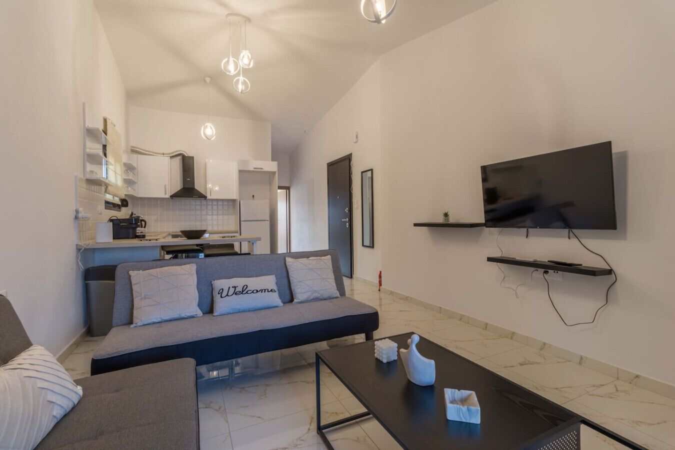 A modern living room with a grey sofa, a coffee table, and a flat-screen TV mounted on the wall.